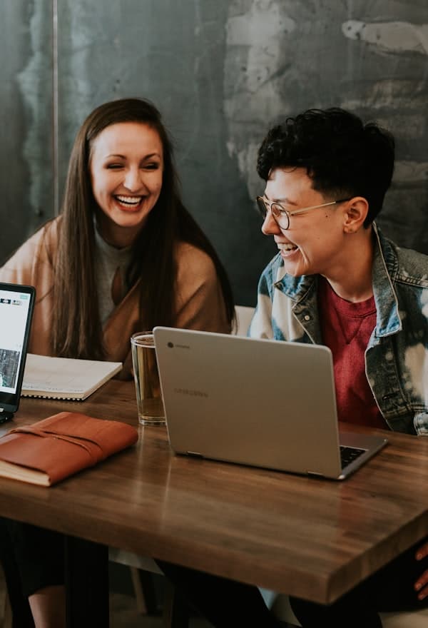 Two students laughing while building an app on a laptop